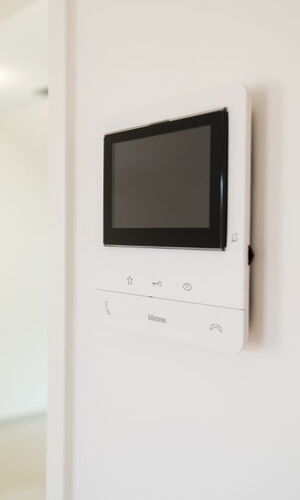 Wandmontiertes Videogegensprechanlagegerät mit Bildschirm und Tasten in einem hellen Innenraum