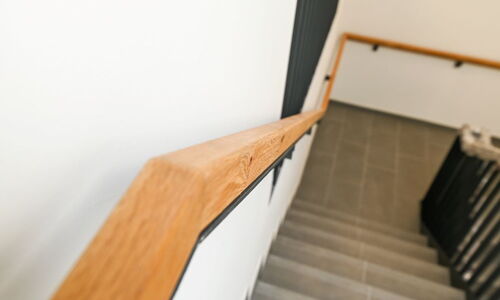 Holzhandlauf an einer Treppe mit grauen Stufen und schwarzem Geländer