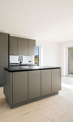 Moderne Küche mit grauen Schränken, Kücheninsel und großem Fenster mit Blick auf Grünfläche