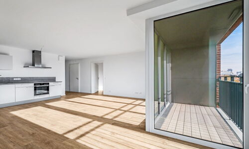 Helles, leeres Wohnzimmer mit offener weißer Küche und großem Fenster zum Balkon mit Blick auf Stadt